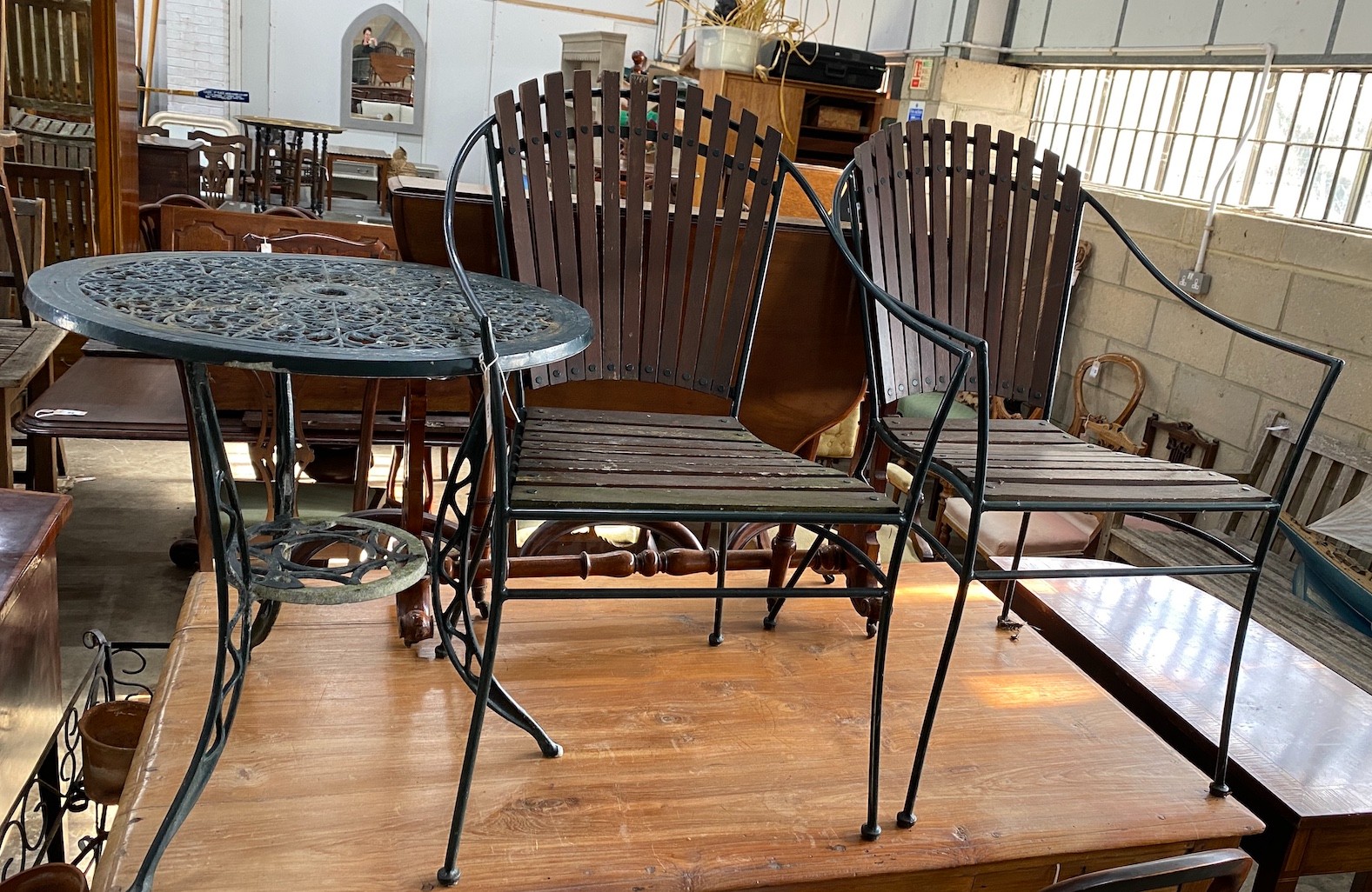 Two wrought iron slatted garden chairs, a circular table and a wrought iron pot stand